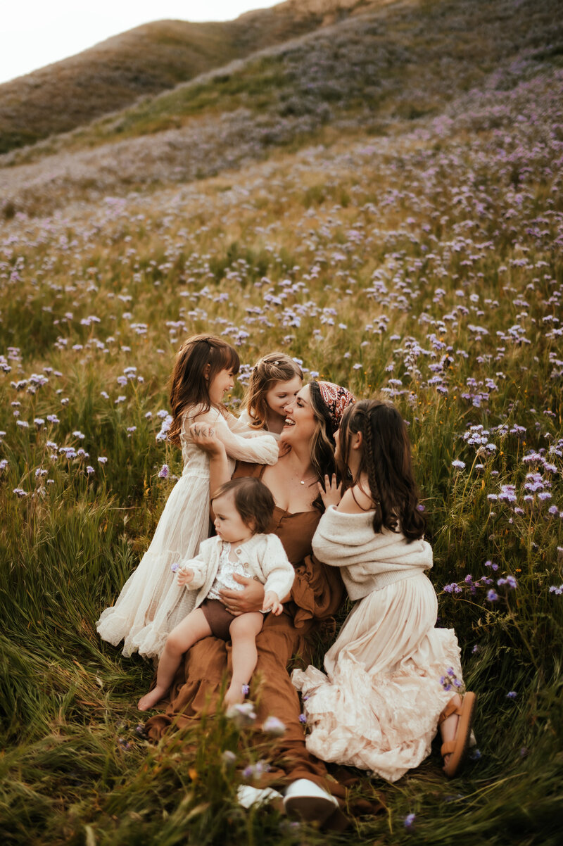 A mother snuggling her four daughters in a field of wildflowers.