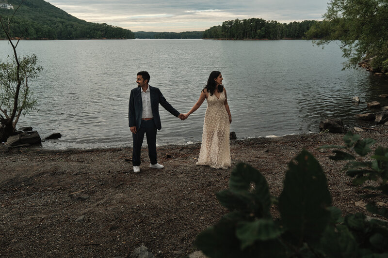 Eloping couple holding hands with a lake behind them