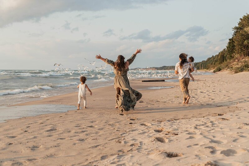 Family chasing seagulls along shoreline photographed by West Michigan family photographers