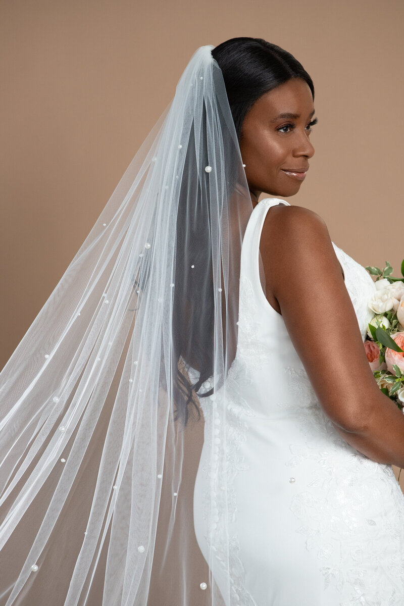 Bride wearing chapel length veil with lots of pearls and holding a white and blush bouquet