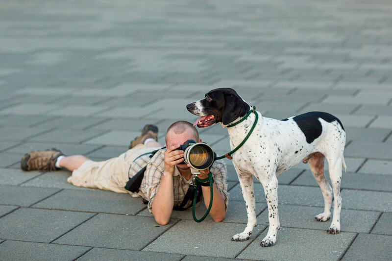 Travis Stitt photographing while holding the leash for a dog during an engagement session, capturing a candid and heartwarming moment that showcases his versatility and care for including pets in stunning couple photos.