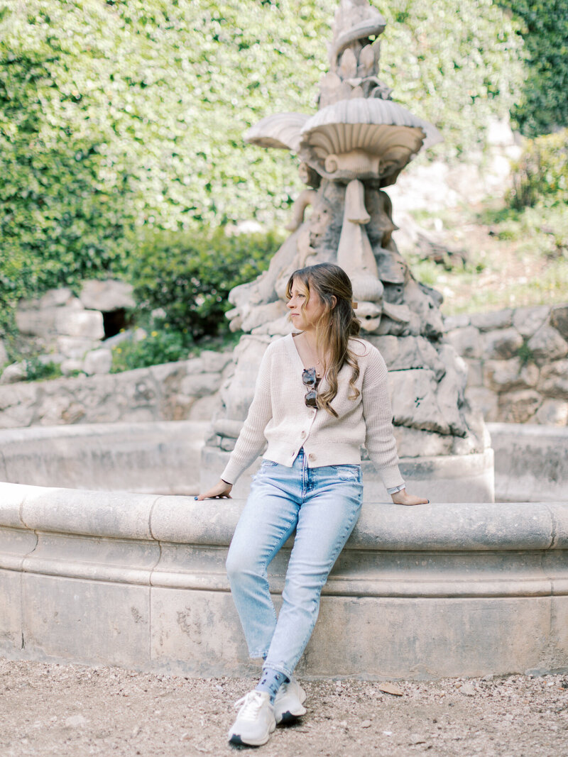 Photographer Little Rock Bailey Feeler sits on edge of Croatian fountain in cream sweater and jeans