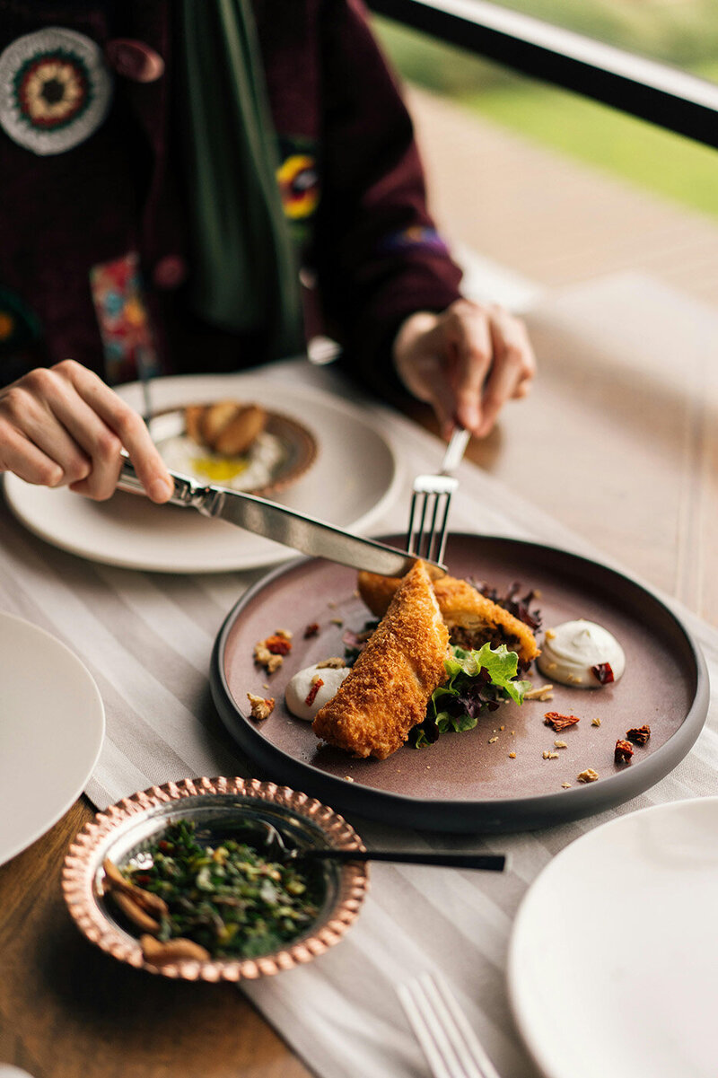 Eat Beyond Labels Owner, Christy, in striped pants strolls through a bustling, dimly lit market. She appears relaxed as she browses various packaged goods on display.