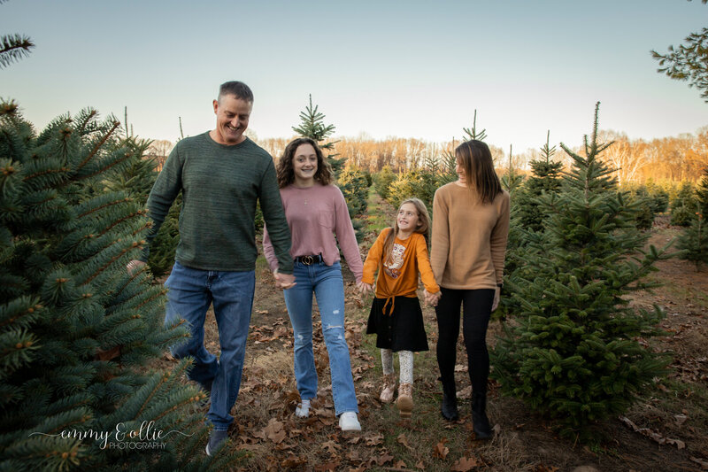 family of four walks towards camera holding hands and smiling at westman's tree farm in dexter michigan