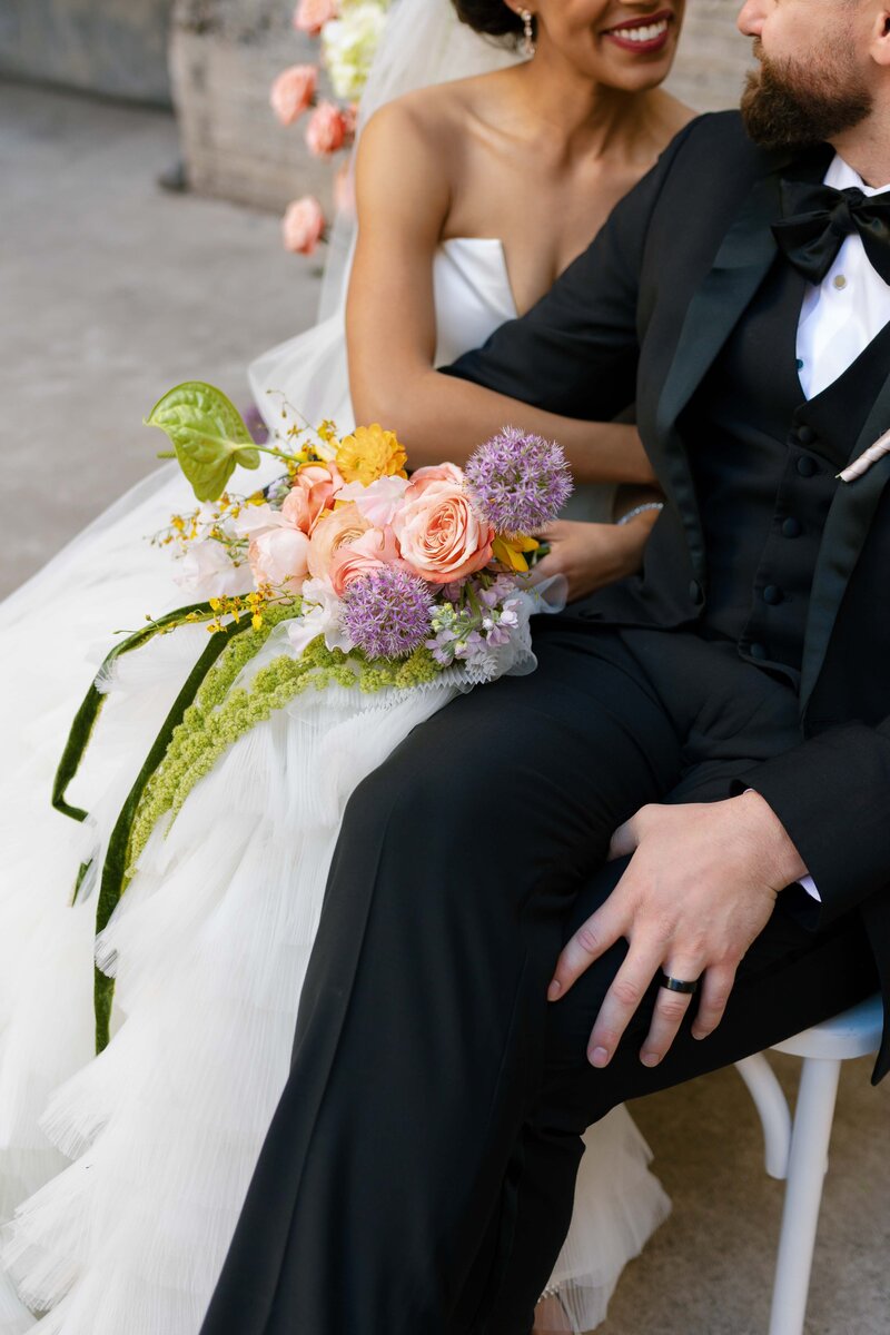 Bride cuddles her groom while holding her colorful bouquet.