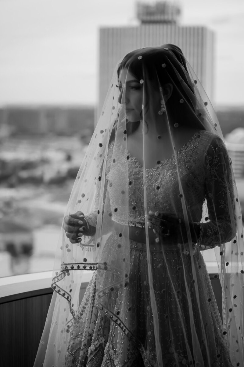 Black and white photo of bride in her wedding gown looking out the window.