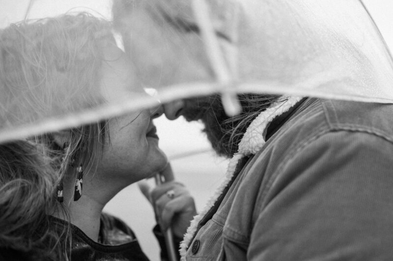In the rain, a couple kisses tenderly under an umbrella, surrounded by droplets that enhance their intimate moment.
