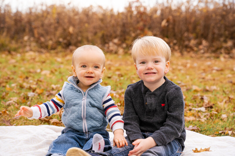 Siblings ages 3 and 1 sitting next to each other in the fall weather at Sharon Woods in Westerville, Ohio.