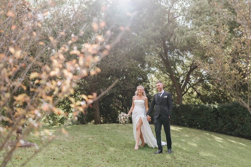 Bride and groom walking through gardens on a lawn in golden light