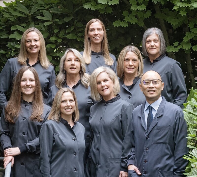 Kao Dental staff smiling at camera in grayish blue dental uniforms outdoors in front of green shrubbery