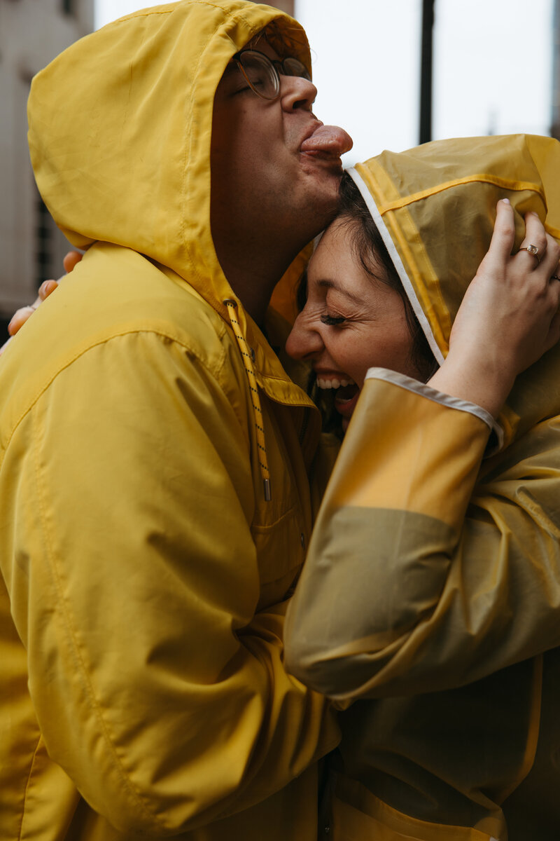 couple laughs in the rain in matching yellow rain coats
