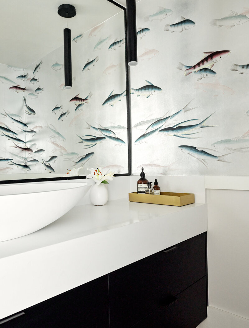 A minimalistic powder room design featuring  a bright white countertop space, black pullout drawers, and de Gournay wallpaper depicting an intricate swimming fish design