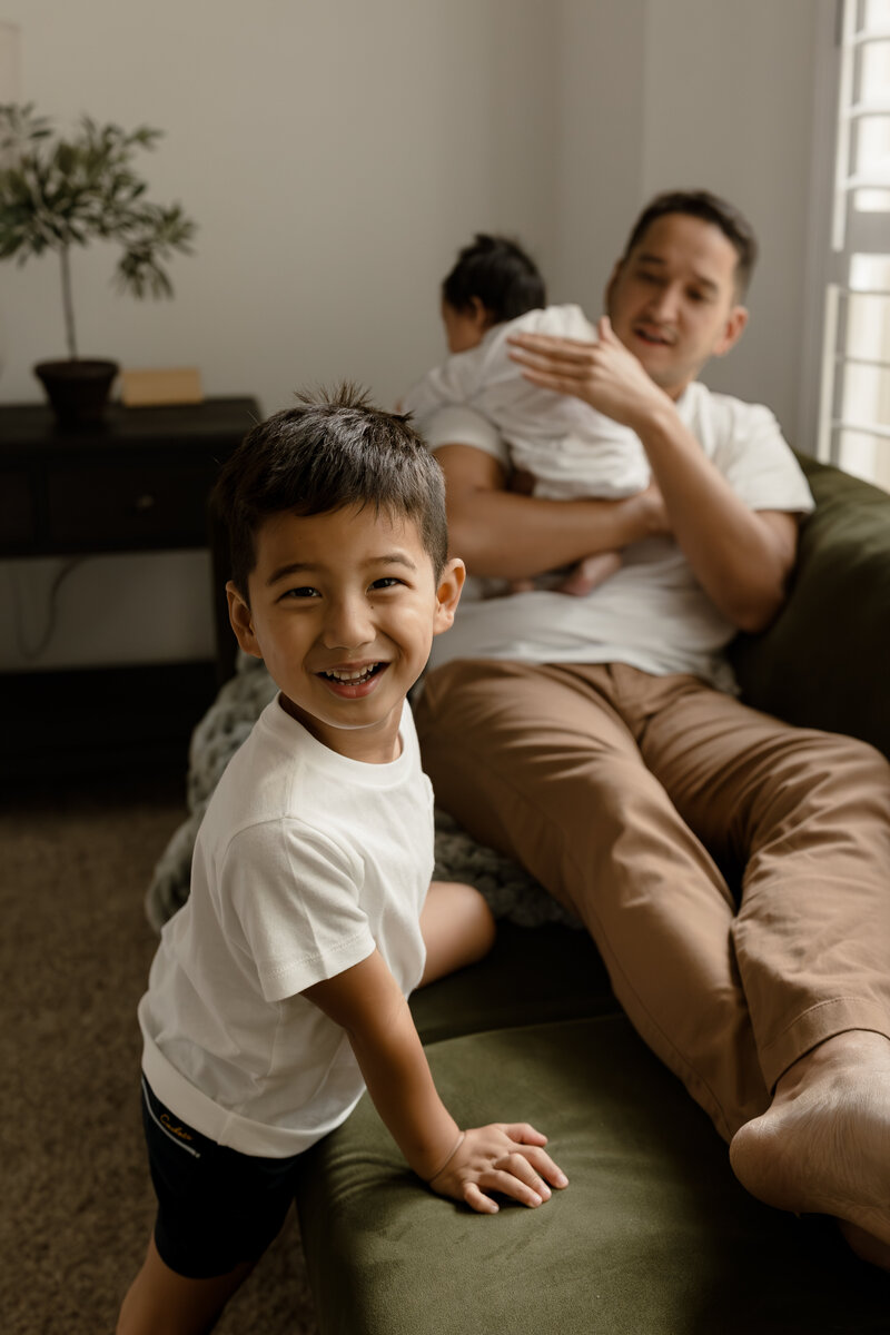 toddler boy looking at camera while dad holds newborn 