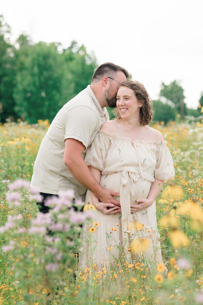 Expecting parents embracing in a field of wildflowers during their louisville maternity photos taken by missy marshall