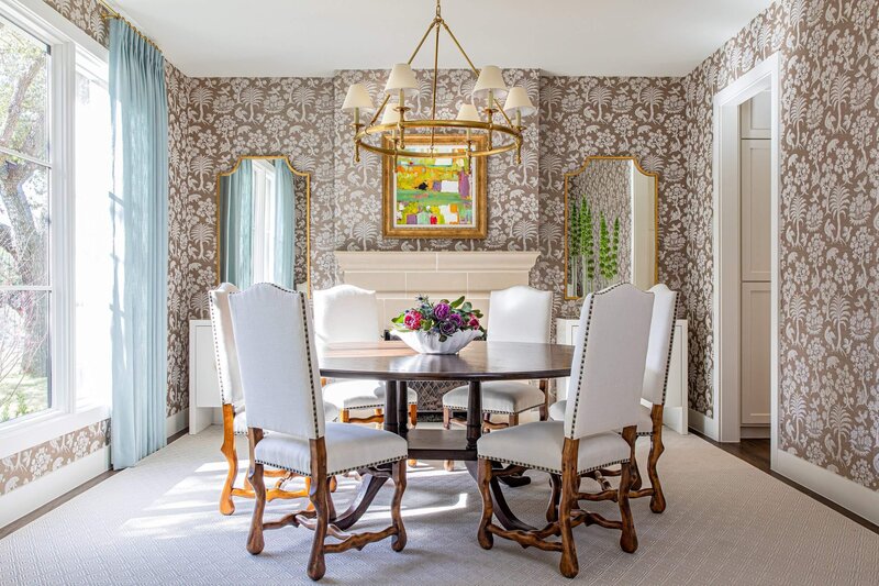 A white kitchen with white chairs and blue upholstered fabric around a white island styled with florals and fruit.