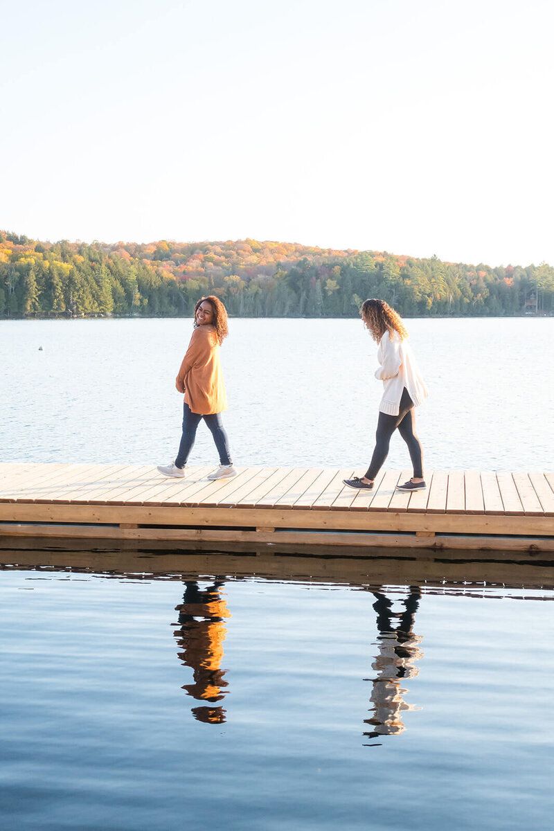 Two women laughing and walking down a dock on a lake . There is a moutain with fall foliage in the background. The words "you can find your freedom" are overlayed on the image.
