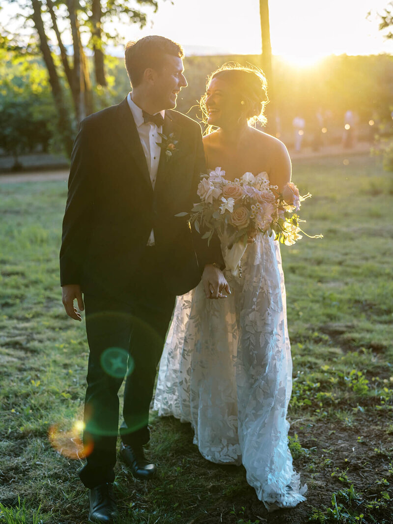 A bride and groom smile at each other with sunlight shining through, representing an example of work from Heather's wedding portfolio. 