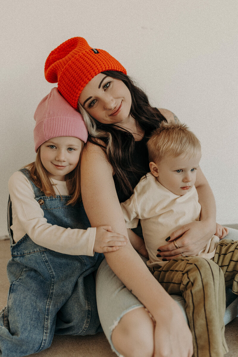 Mother in a red beanie snuggling her two young children.
