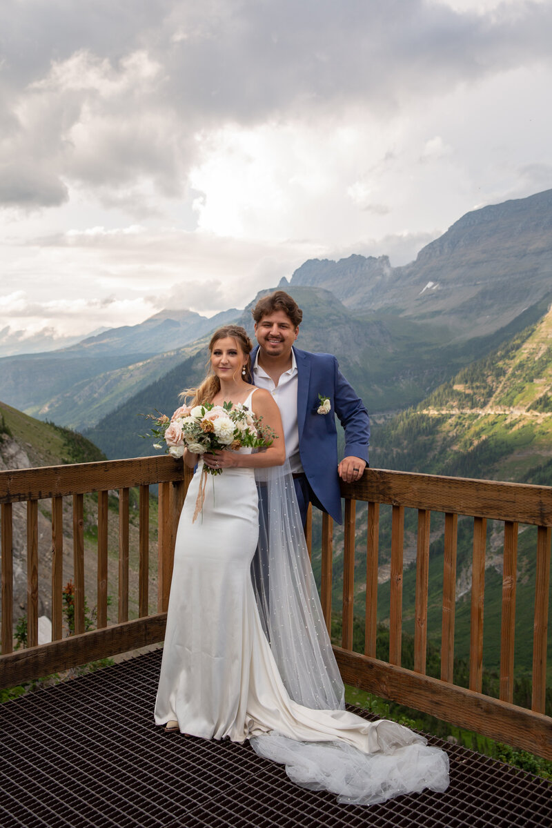 Bride & Groom stand on a viewing deck overlooking the peaks of Glacier National Park
