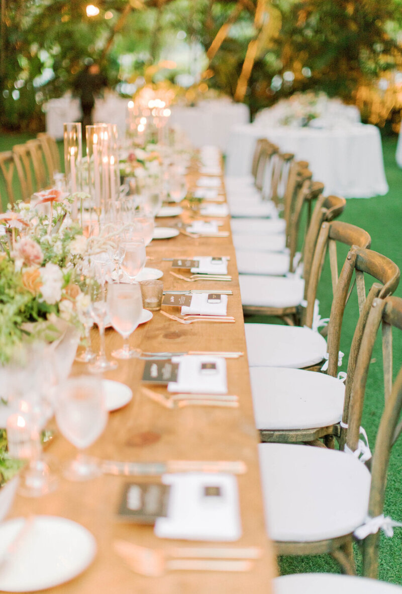 Outdoor wedding reception with long wooden table and colorful floral and candle centerpieces