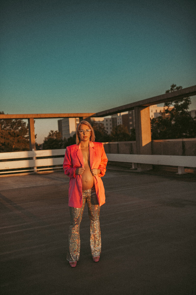 Pregnant woman in a pink blazer and sparkly bell bottoms showing off her baby bump.