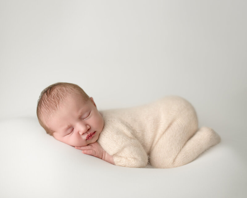 Newborn posed session, baby girl in the tushie up pose on white background wearing a soft knit romper

