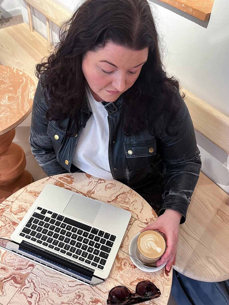 Martina Menzini, writer, editor, and consultant, working on laptop at marbled cafe table.