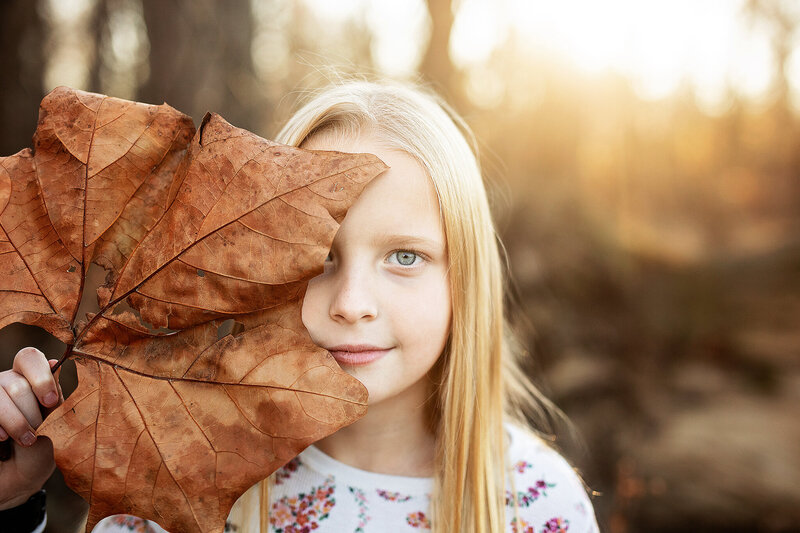 Young girl hiding behind  a large sycamore leaf