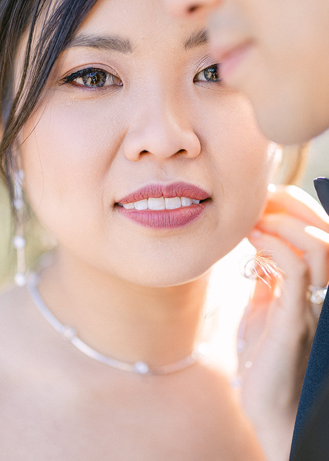 This close portrait captures a tender moment in Calgary, Alberta, where a bride looks directly into the camera, held closely by her fiancé. The emotional depth and connection between the couple are palpable, framed by the warmth and love of their embrace.
