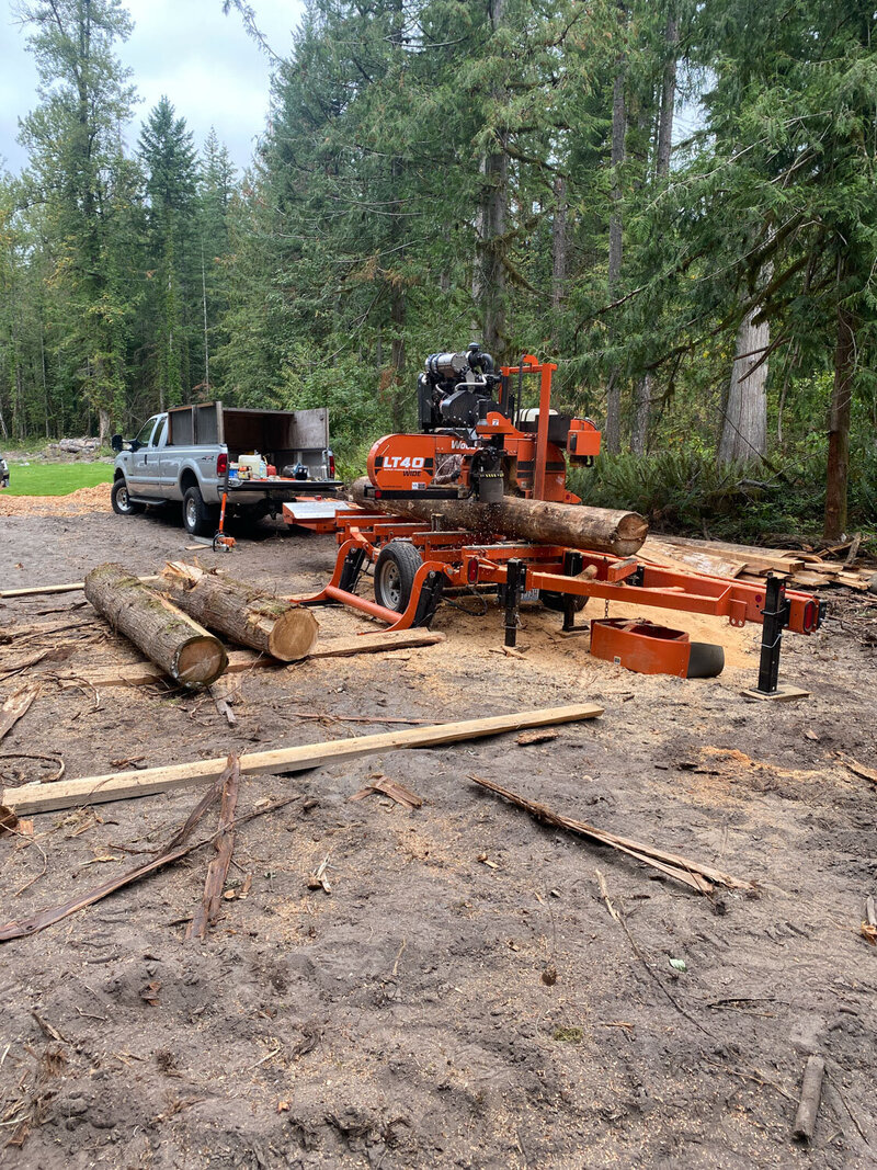 Logging machine cutting wood near a parked truck
