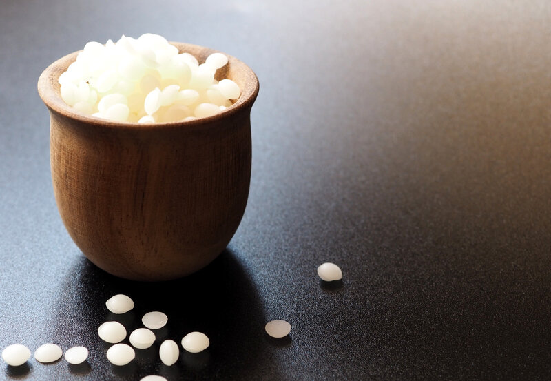 Close-up of spa essentials including bottles of massage oil, rolled towel, candles, and smooth stones on a wooden surface.