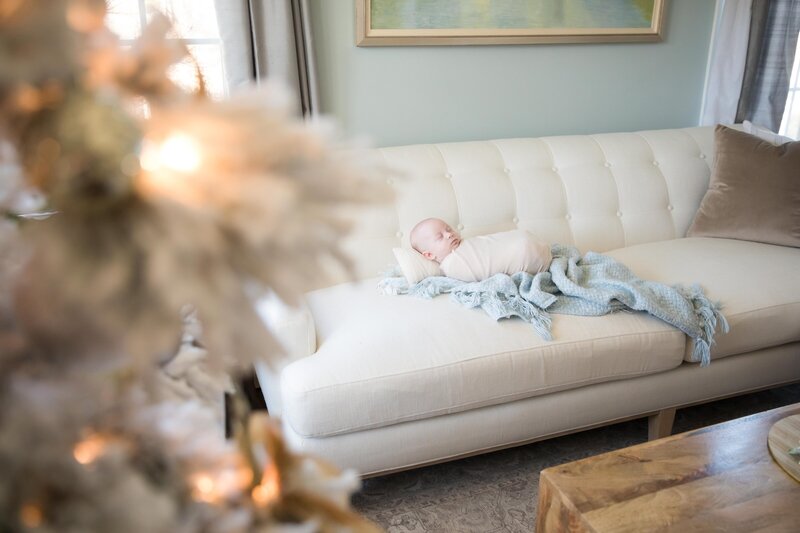 Baby sleeping on couch with Christmas tree in the foreground waiting on Santa 2024