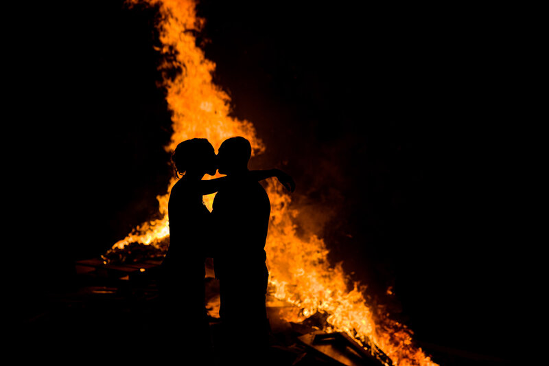 Silhouette of a couple standing in front of a glowing fire during their backyard wedding, highlighting intimate wedding style.