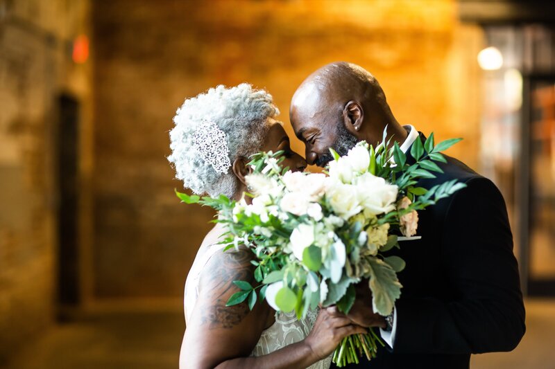 married couple kissing behind bouquet