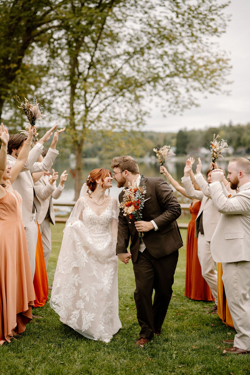 Newlywed couple walking away hand in hand as guests cheer them on during their outdoor New York City wedding, captured by NYC wedding and elopement photographer Dom Augustine.