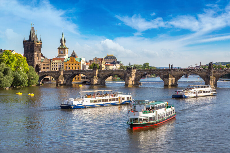 Scenic view of a small luxury river cruise boat gliding past a European village, symbolizing curated, slow travel on the water.