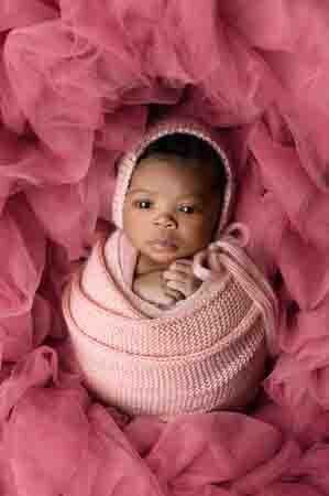 Newborn photography — baby girl in pink swaddle and bonnet, eyes open and surrounded by pink tulle