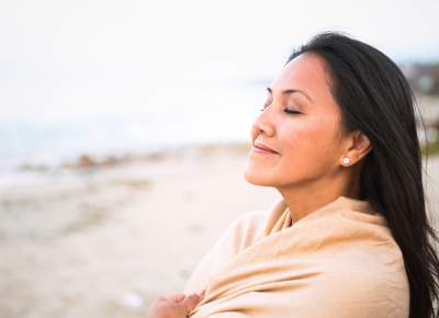 woman on beach with scarf and eyes closed  calmly smiiling