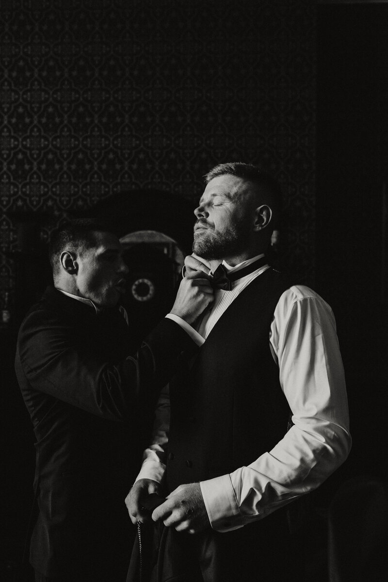 Black and white still of a groom having his bowtie done up at Huntsham Court