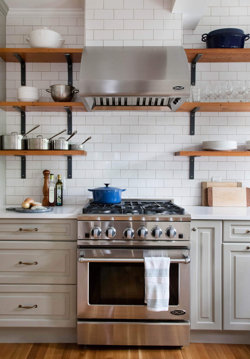 Traditional kitchen design in Boston transforms a remodeled Winchester home with light green cabinets and open shelving made from reclaimed wood for a warm touch.