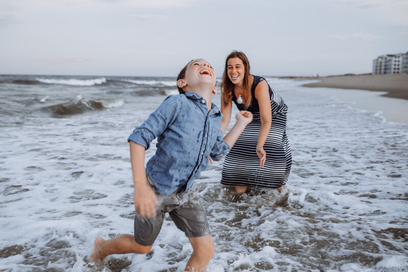 A mom and son splash in the water at the beach.