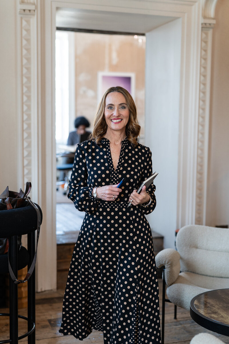 woman walking into the room in black and beige polka dot dress, smiling