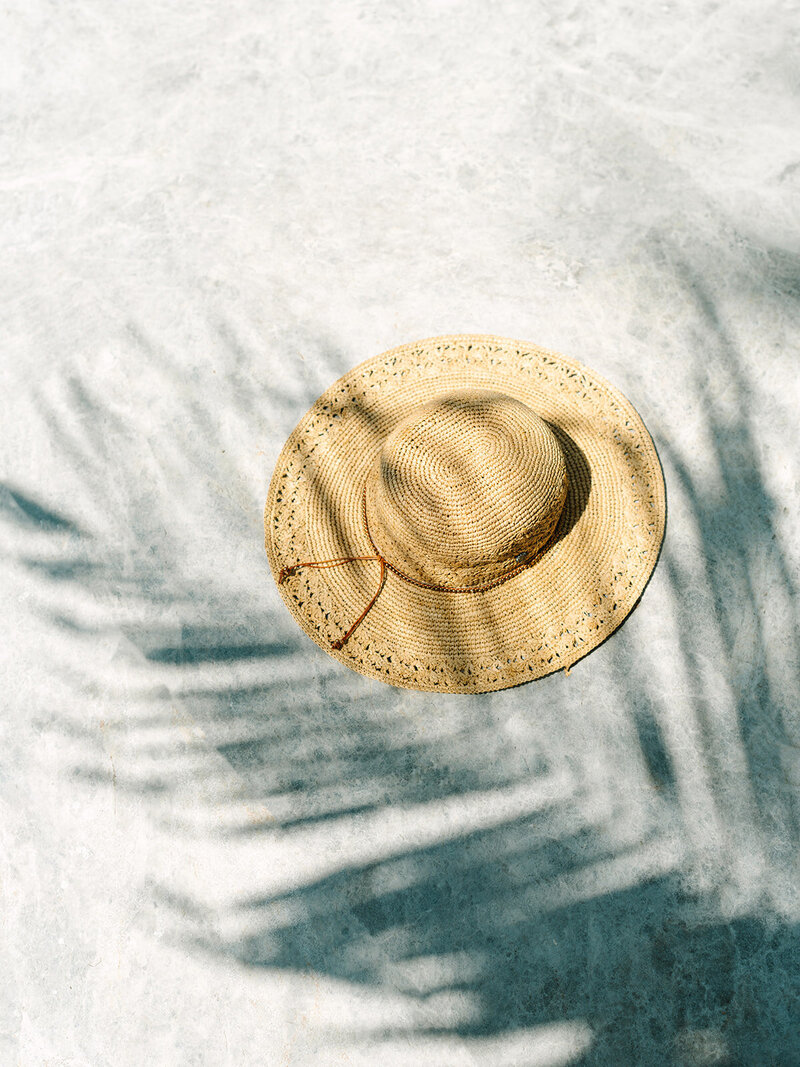 Straw hat laying on the ground with palm tree shadow over ti