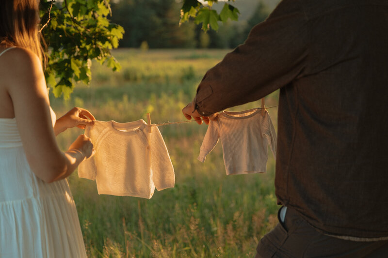 couple hanging baby clothes on clothesline for maternity session in pei