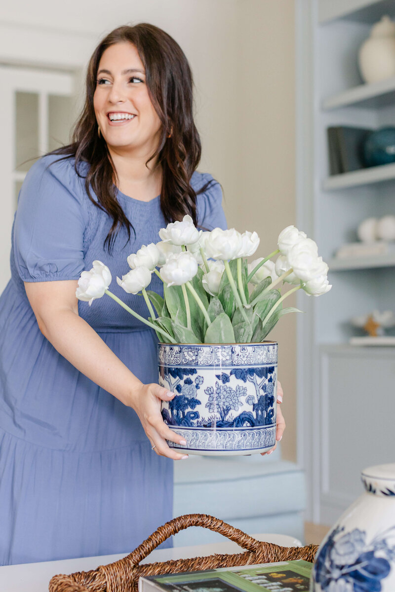 A lady in a blue dress holding a vase with white flowers