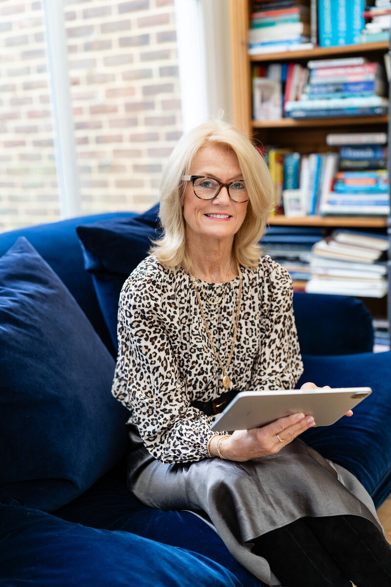 woman in leopard print blouse sitting on a dark blue soffa with tablet in her hands