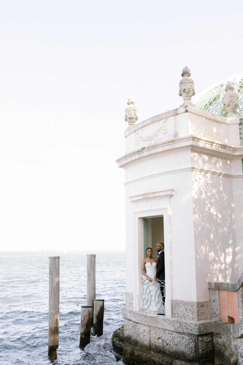 Bride and groom pose on balcony next to water at Vizcaya Museum & Gardens