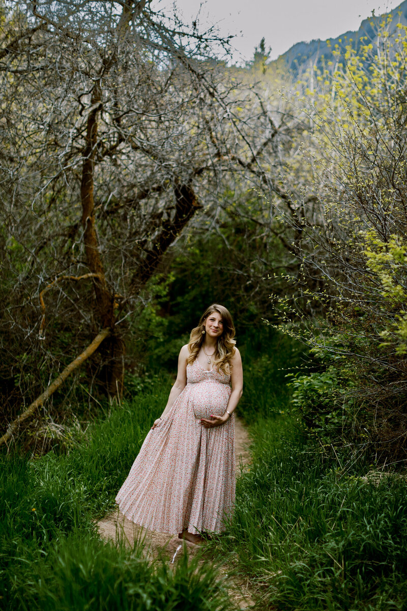 photo of a boulder colorado pregnant woman in a dress on a trail in spring