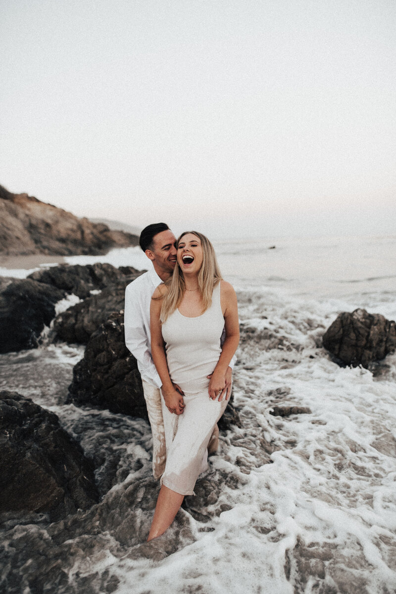 woman and man leaning on rock on beach