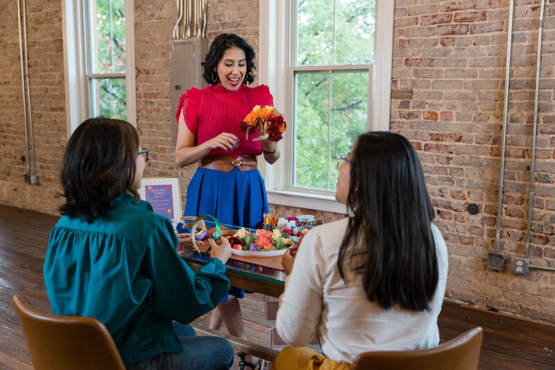 The conversation of empowerment as our artist guides two women in crafting flower crowns. Immerse yourself in a world of colors and textures on the table, where creativity blossoms.